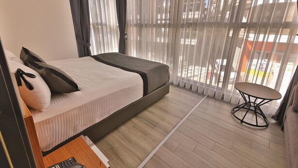 A hotel room with a bed, a small table, and large windows with curtains. - BUCA MAT HOTEL BY TAHTALI (Izmir)