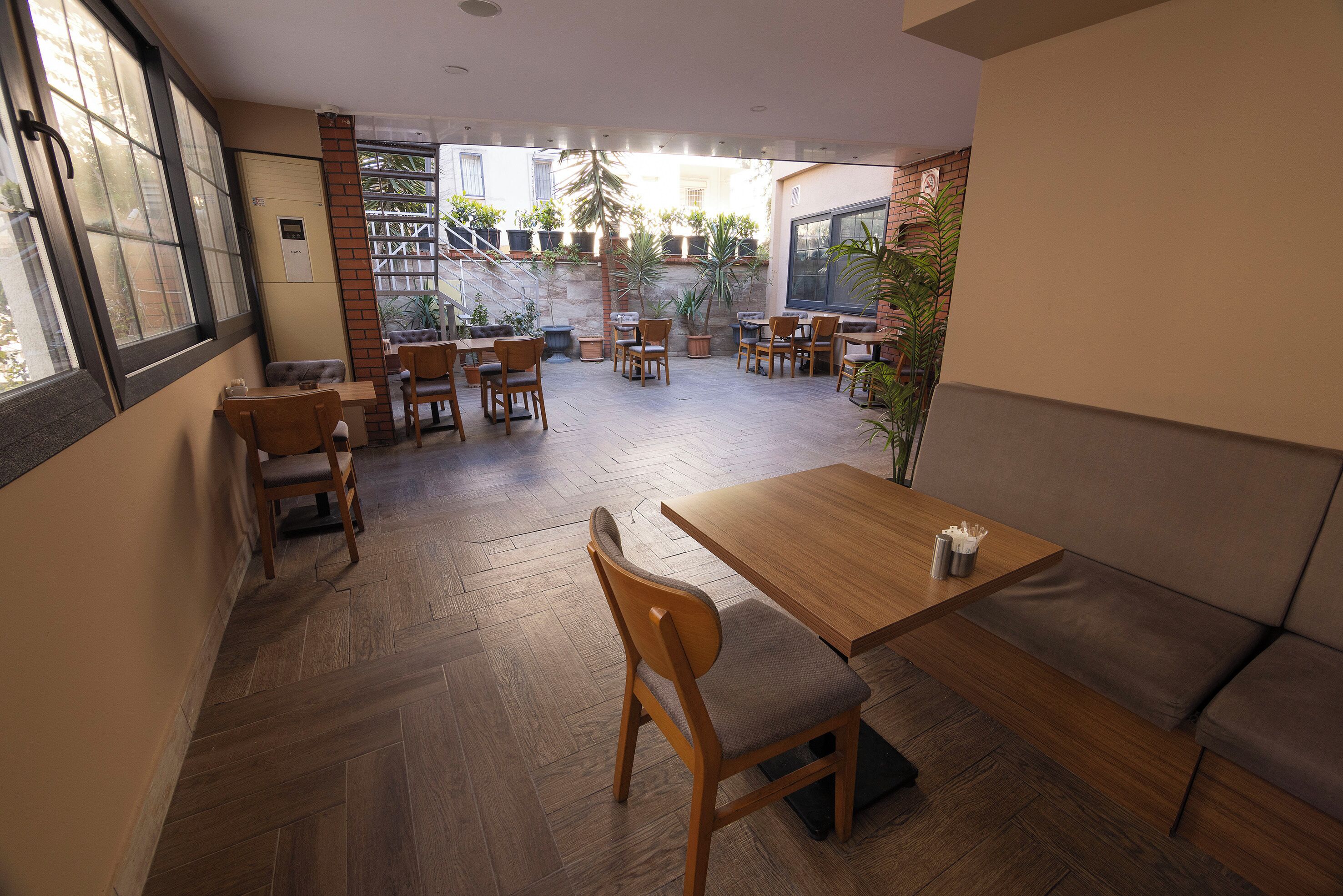 A restaurant with wooden flooring, multiple tables and chairs, a sofa, and potted plants.