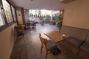 Un restaurante con piso de madera, varias mesas y sillas, un sofá y plantas en macetas.