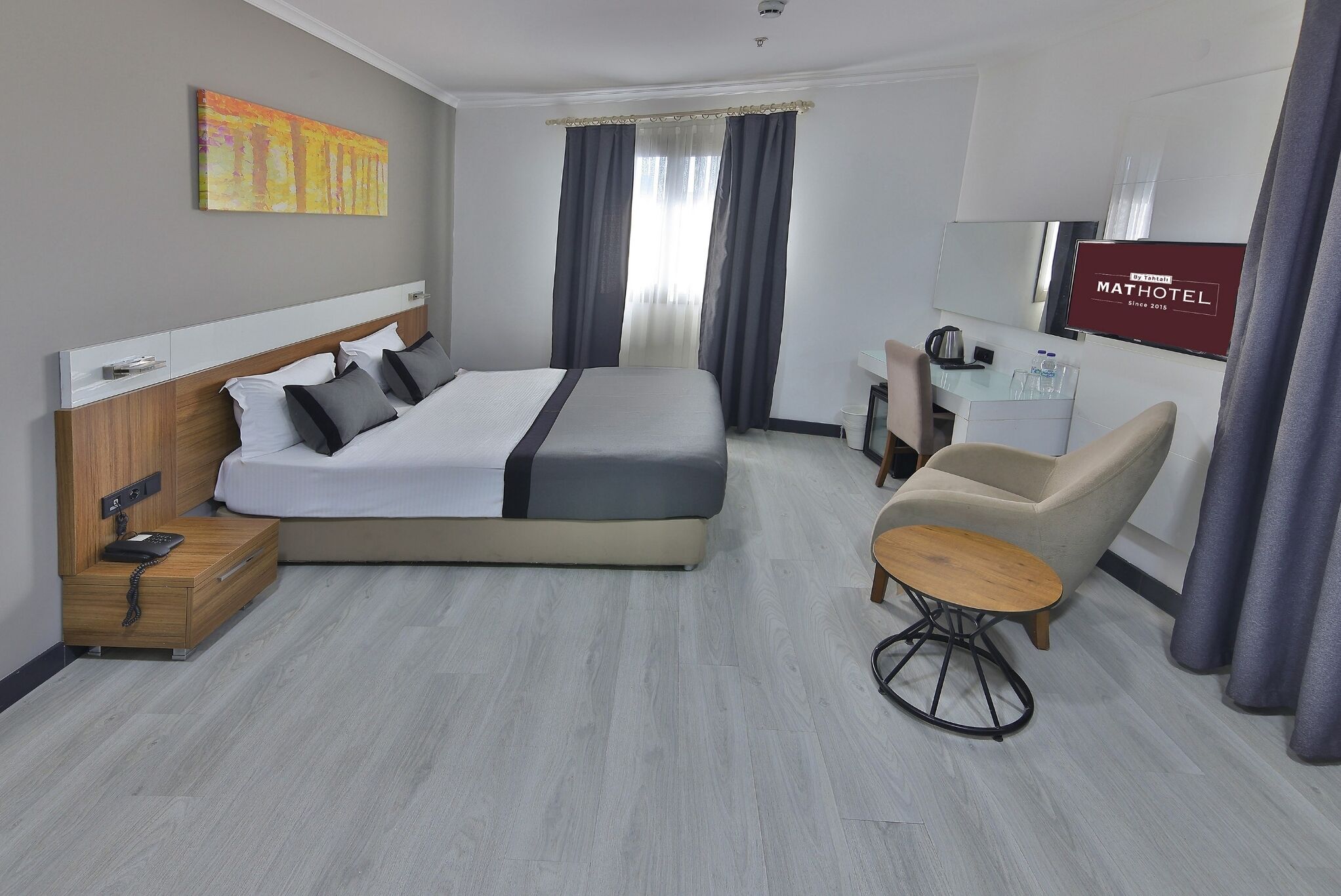 A modern hotel room with a large bed, a desk, a chair, and a TV.