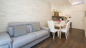 A modern living room with a grey sofa, white chairs, and a dining table.