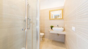 A modern bathroom with a glass shower enclosure, a toilet, and a sink with a gold-framed mirror above it.