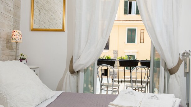 A bedroom with a bed, a window with curtains, a chair, and a table with towels.