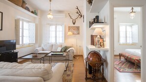 A spacious living room with a sofa, coffee table, and a globe as a centerpiece. There are multiple windows providing natural light, and a bookshelf filled with books and decorative items.