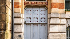 En byggnadsfasad med en stor, utsmyckad dörr som bär inskriptionen ”BEREY’S BUILDINGS” och ett fönster ovanför.