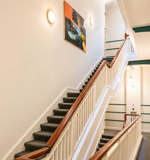 A staircase with wooden handrails and carpeted steps, leading to a landing with a light fixture and a wall-mounted painting.