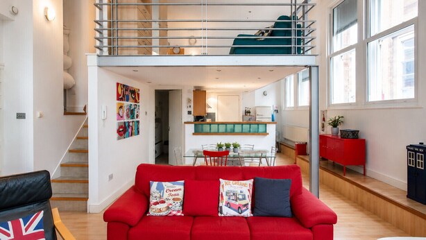 En modern lägenhet med en röd soffa, ett matområde, ett kök och ett sovloft.