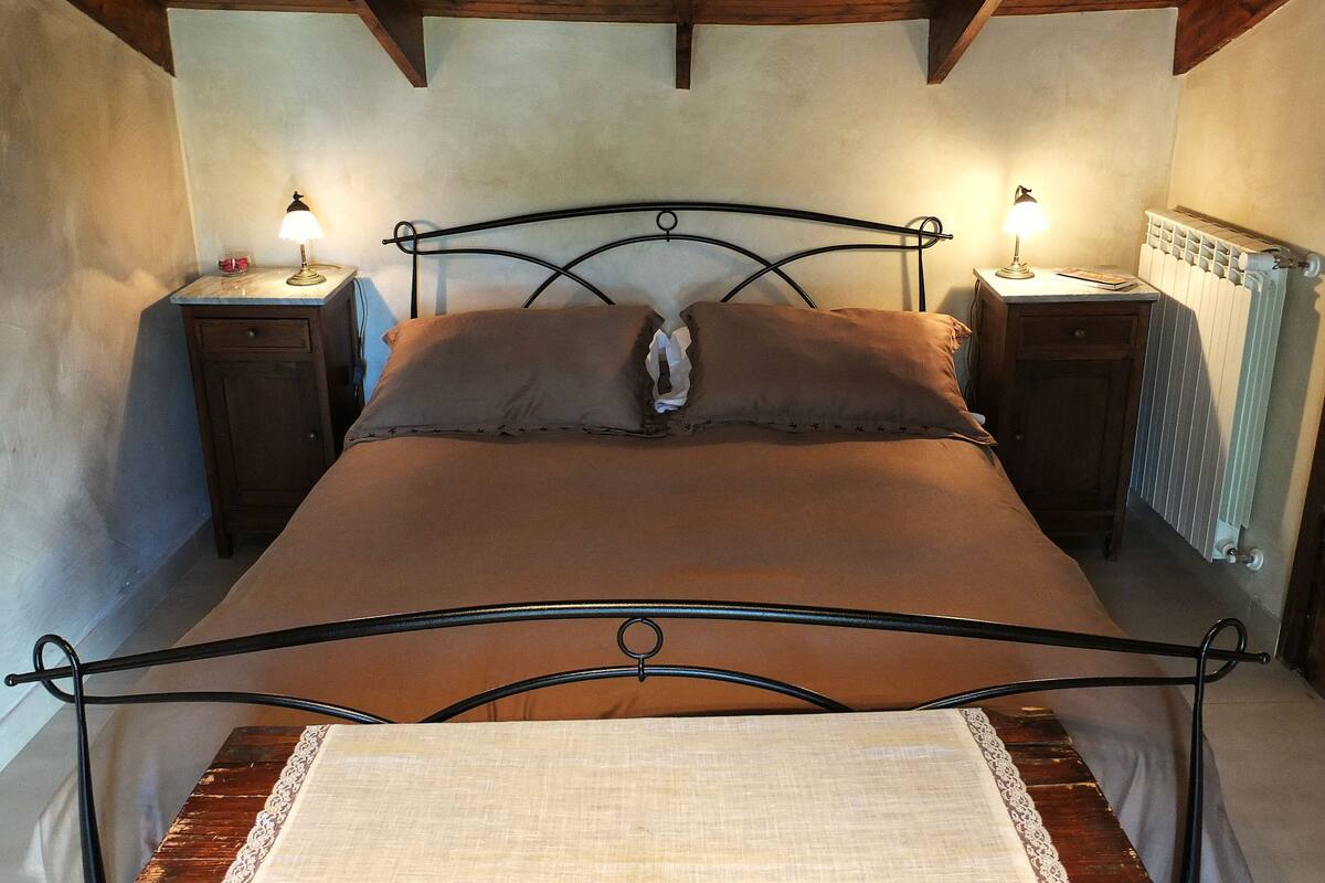 A single bed with a metal frame, two bedside tables with lamps, a wooden headboard, and a radiator.