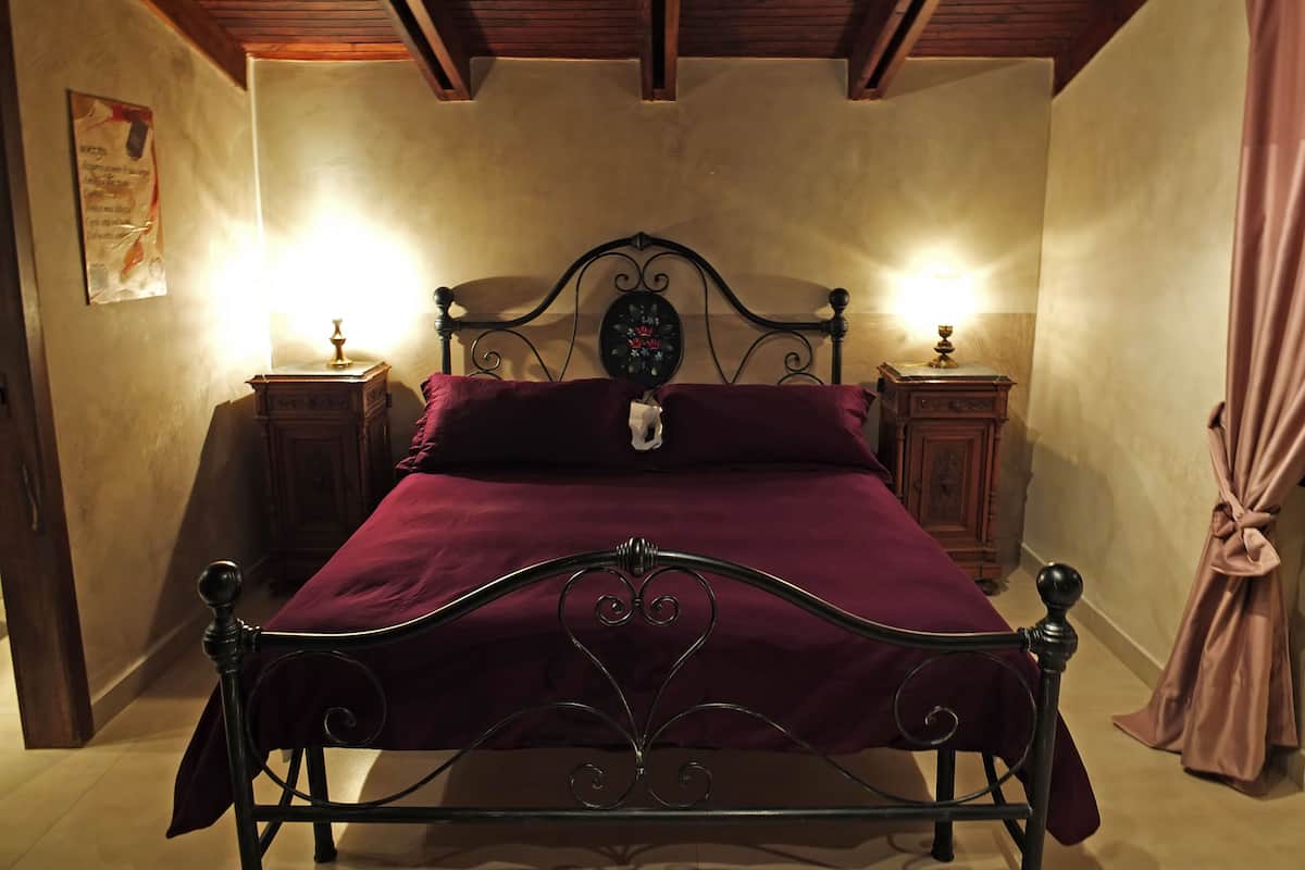 A bedroom with a four-poster bed, wooden headboard, two bedside tables with lamps, and a curtain on the window.