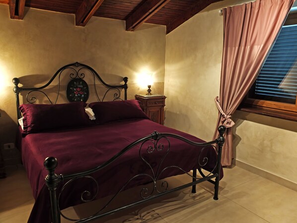 A bedroom with a metal bed frame, a wooden nightstand, a bedside lamp, and a window with curtains.