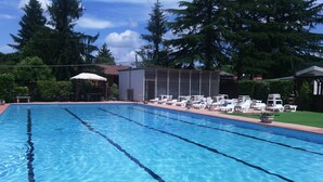 Ein rechteckiger Swimmingpool mit klarem, blauem Wasser, umgeben von Liegestühlen und einem kleinen Gebäude mit rotem Dach.