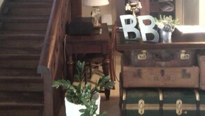 Eine Holztreppe führt zu einem Raum mit einer Lampe, einem Tisch mit einem 'BB'-Schild und alten Koffern.