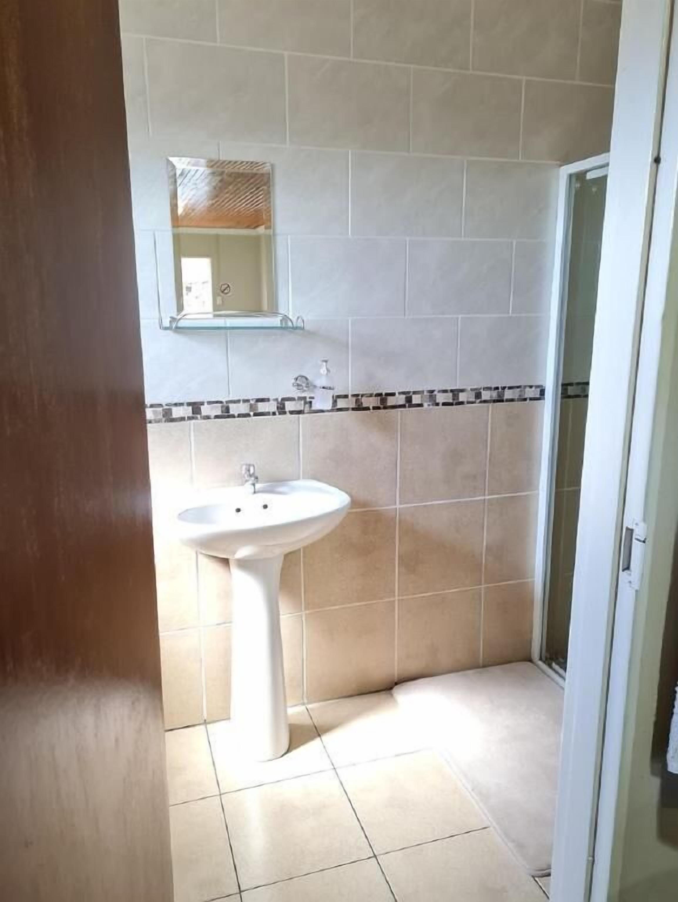 A bathroom with a pedestal sink, a mirror above it, and tiled walls.