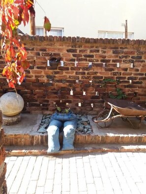 Un muro di mattoni con etichette appese, un vaso in pietra e una bicicletta.