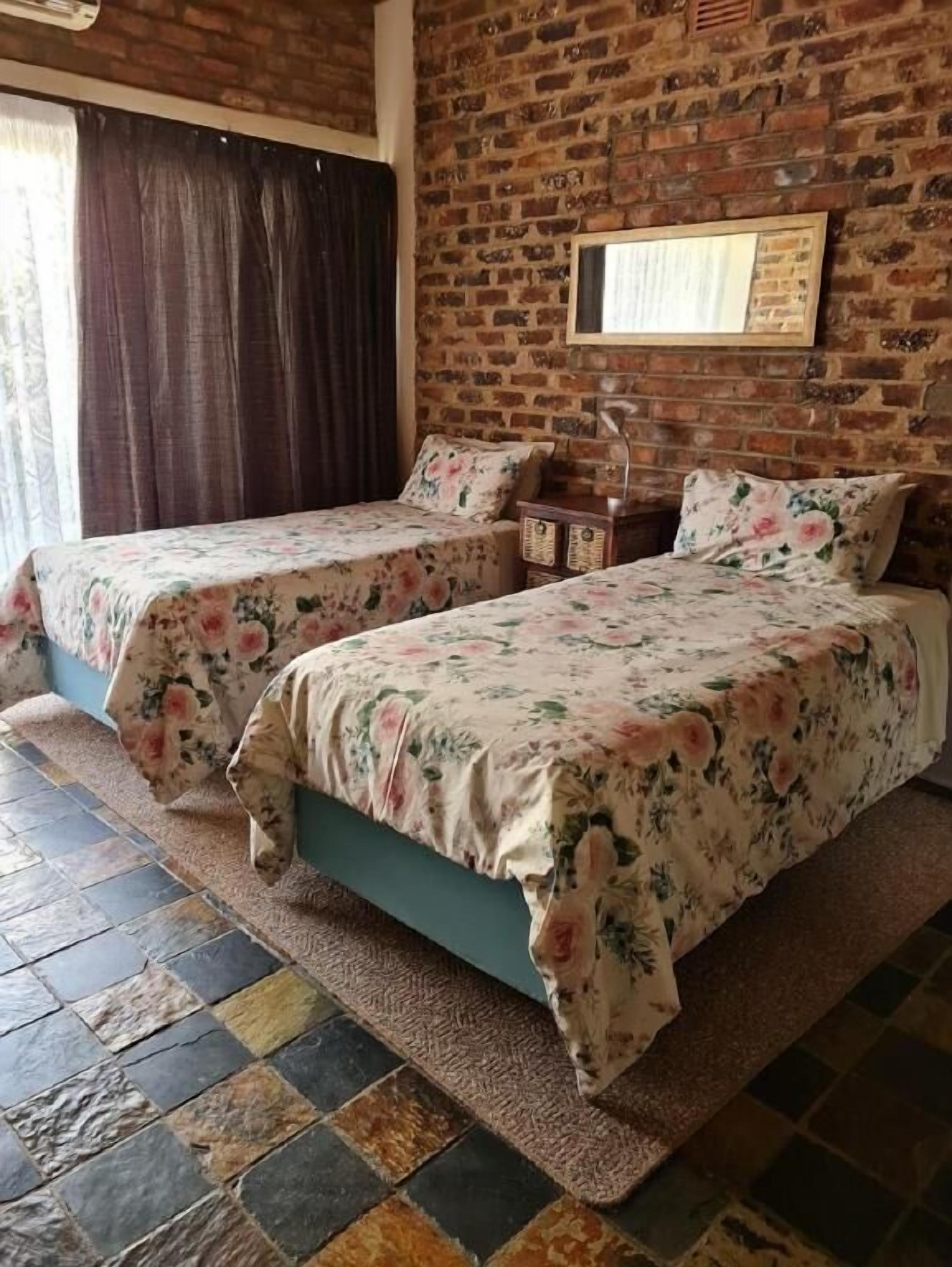 A room with two beds, each with floral bedding, a brick wall, and a window with curtains.