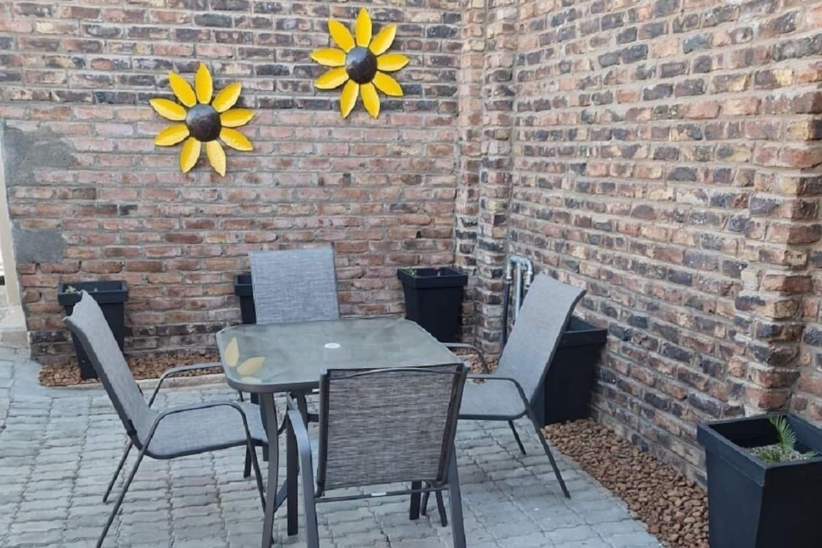 Eine Ziegelwand mit zwei Sonnenblumen, ein Tisch mit vier Stühlen und einem Topfpflanzen.