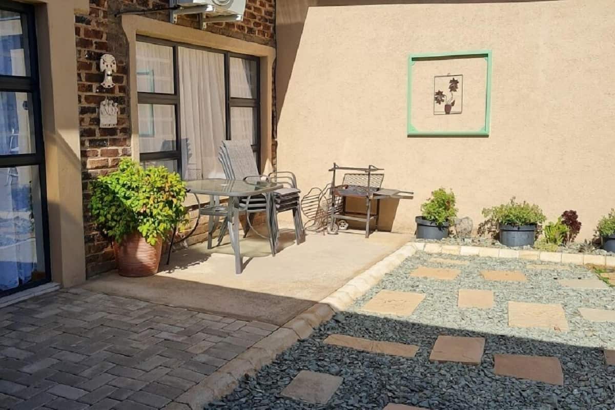 Ein Innenhof mit Backsteinmauer, einem Tisch mit Stühlen, Topfpflanzen und einem kleinen Gartenbereich mit trittfesten Steinen.