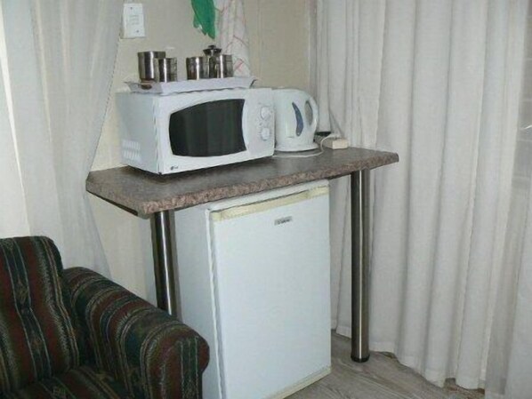 A compact kitchenette with a microwave and a small refrigerator on a metal stand.