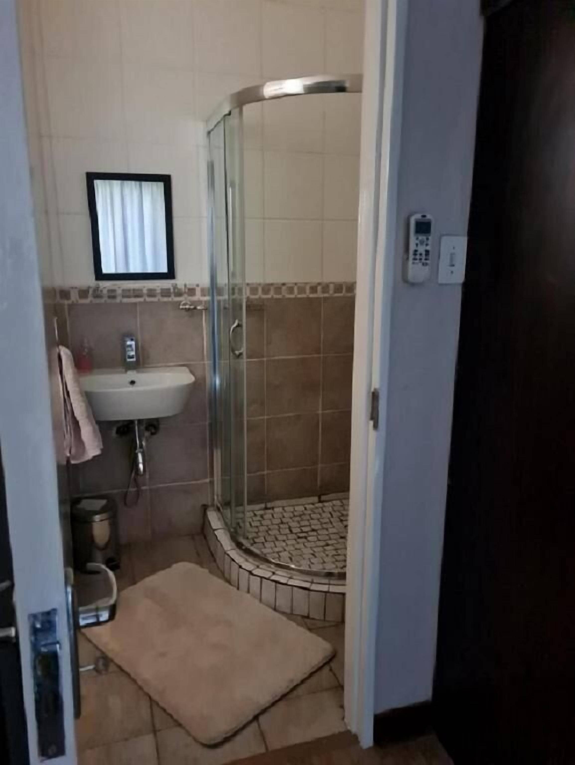 A bathroom with a glass-enclosed shower, a sink, and a small window.