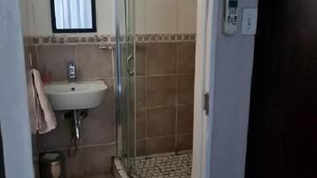 A bathroom with a glass-enclosed shower, a sink, and a small window.