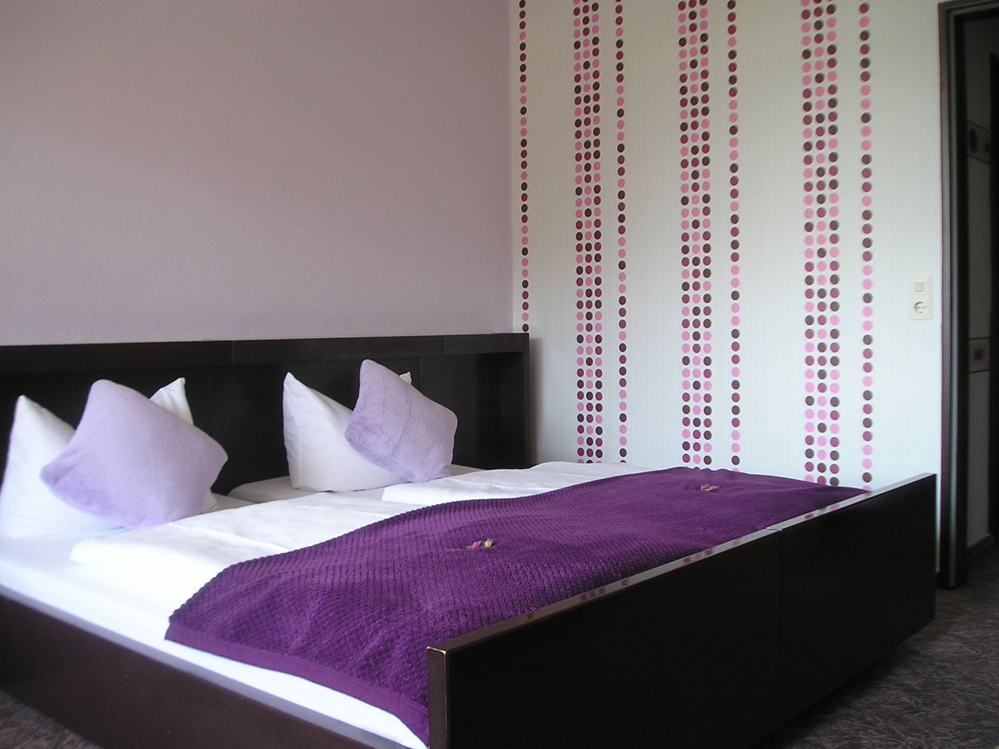 Un lit avec une tête de lit noire, une literie blanche et des touches de couleur violette.