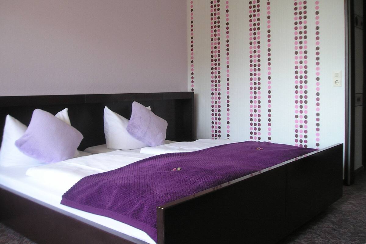 A bed with a black headboard, white bedding, and purple accents.