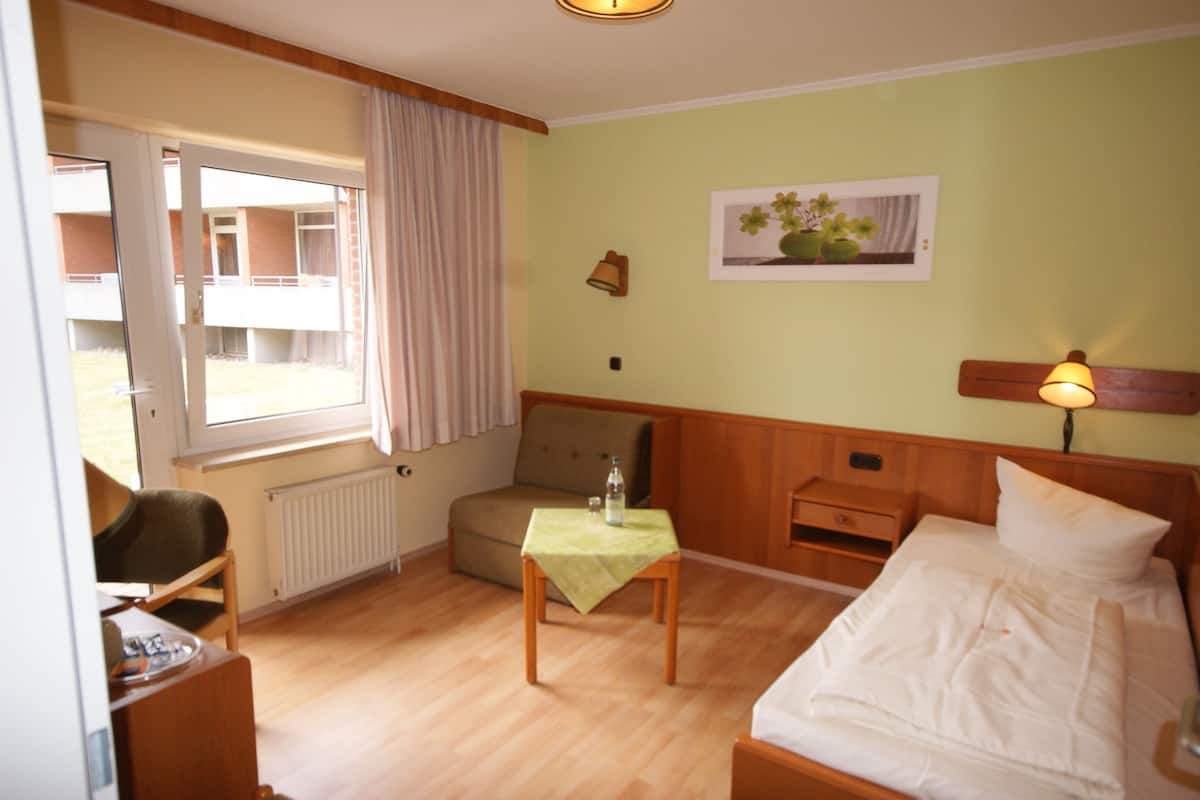 A hotel room with a bed, a small table, a chair, a window, and a view of the outside.