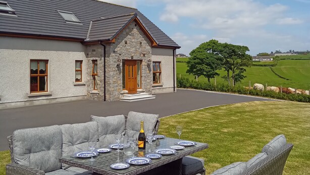 Une maison en pierre avec une allée pavée, un espace extérieur aménagé avec une table ronde et une bouteille de champagne.