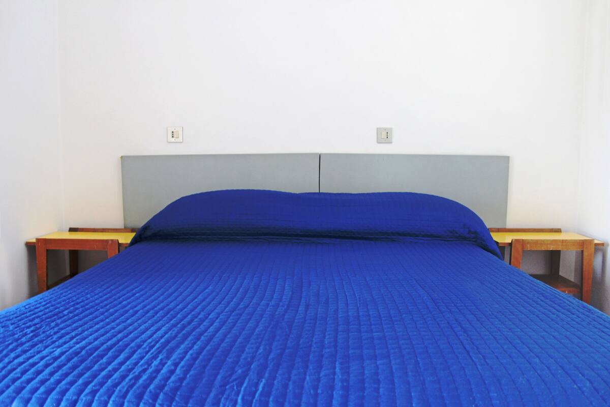 Un lit avec une couette bleue, une tête de lit grise et des tables de chevet en bois.