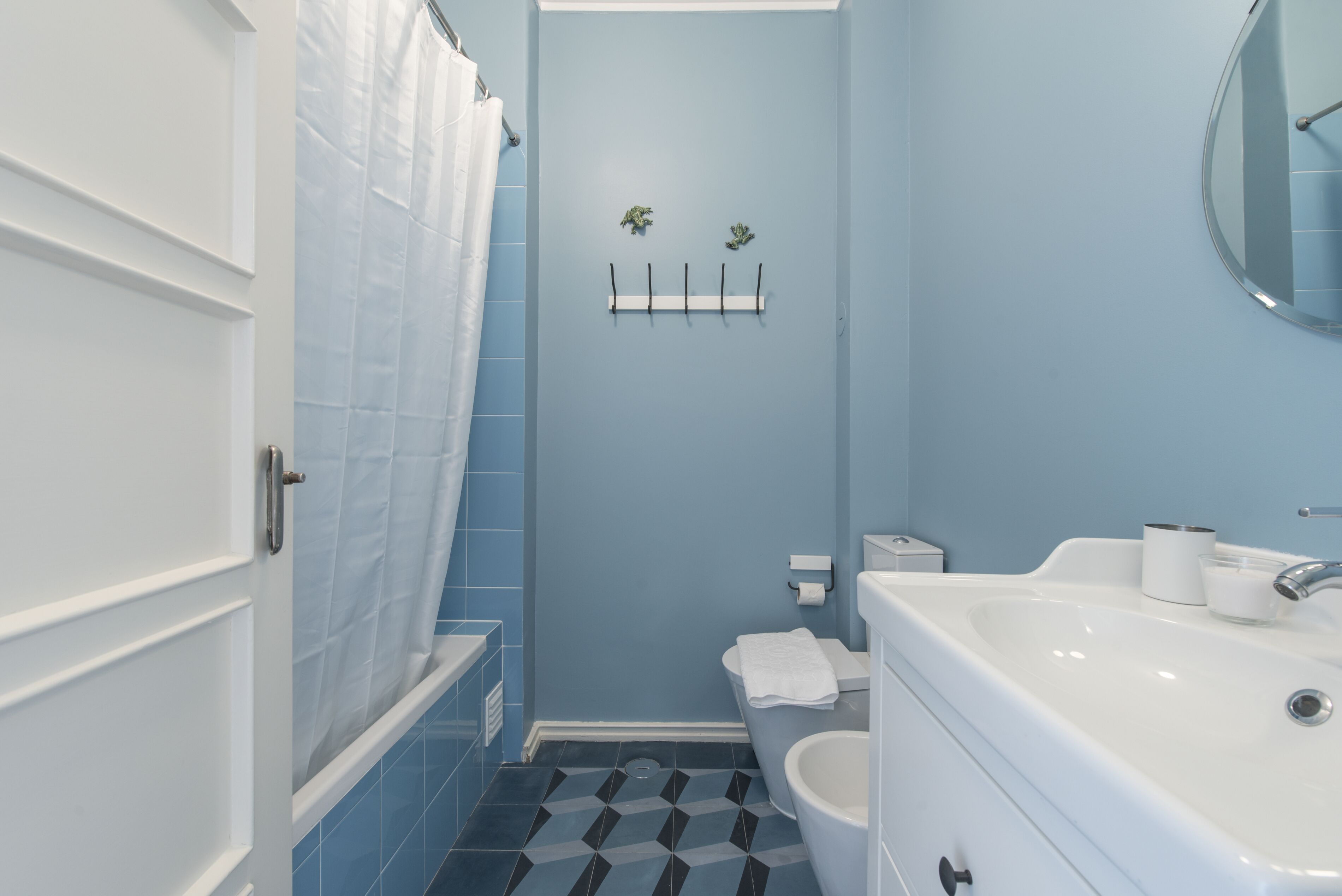 Une salle de bain avec un mur bleu, des accessoires blancs, un rideau de douche, des toilettes et un lavabo.
