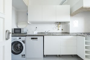 A compact kitchen with a washing machine, microwave, and a sink.