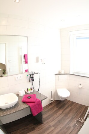 A bathroom with a white sink, a mirror, a toilet, and a vanity with a pink towel. - Gästehaus Stock (Friedrichshafen)