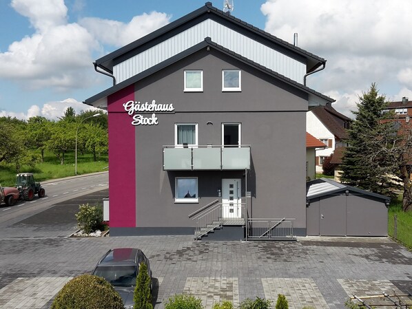 A modern building with a sign reading "Gästehaus Stock" on the side. It features a balcony, a small entrance with a door, and a staircase leading to the entrance. - Gästehaus Stock (Friedrichshafen)