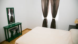 A bedroom with a bed, a green console table with a mirror, and a nightstand with a lamp.