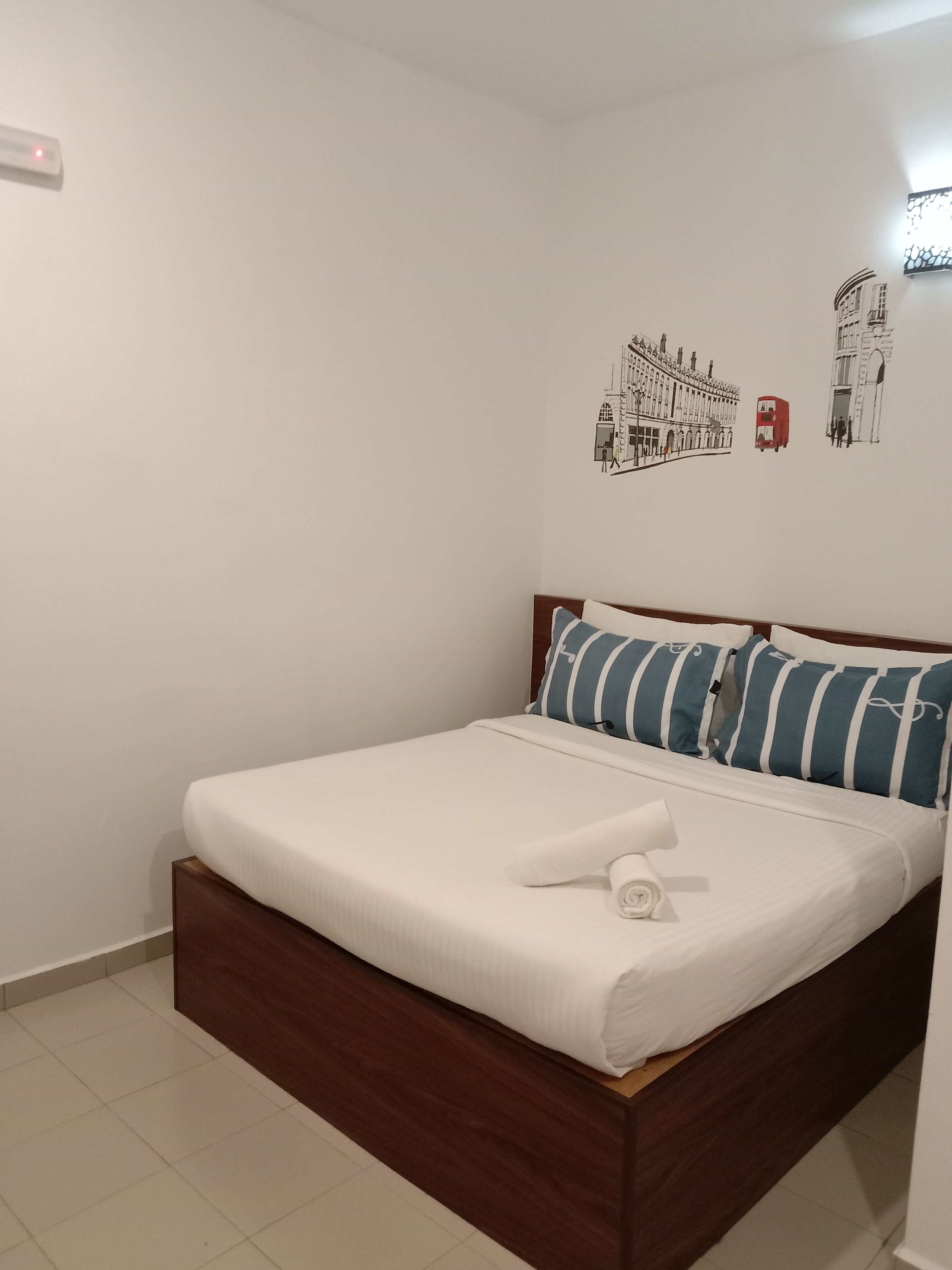 A neatly made bed with a white mattress and blue-striped pillows, a wooden headboard, and a wall with a simple, clean design.