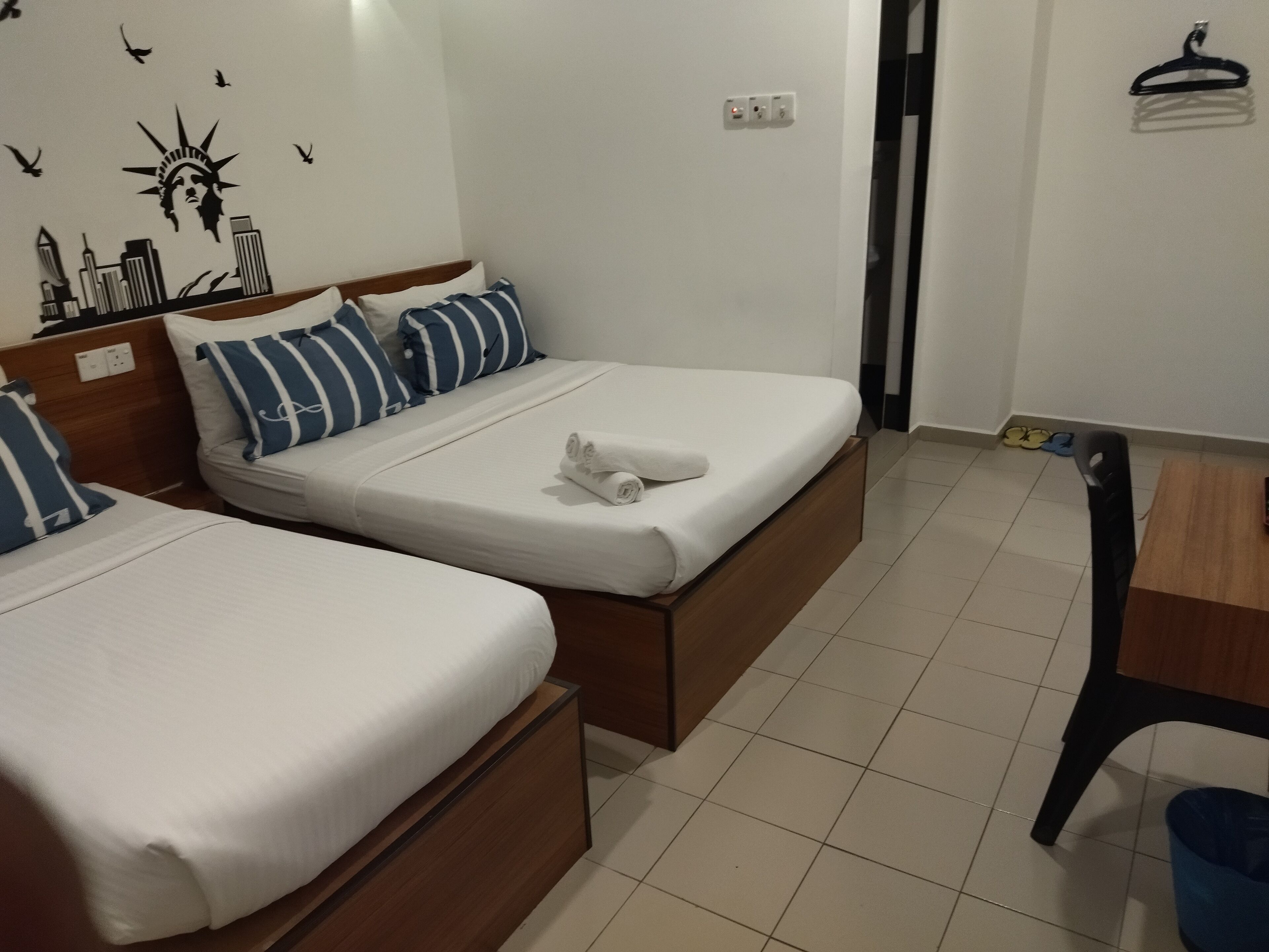 A hotel room with two beds, each with white bedding and striped pillows. There is a wooden table and a chair in the room.