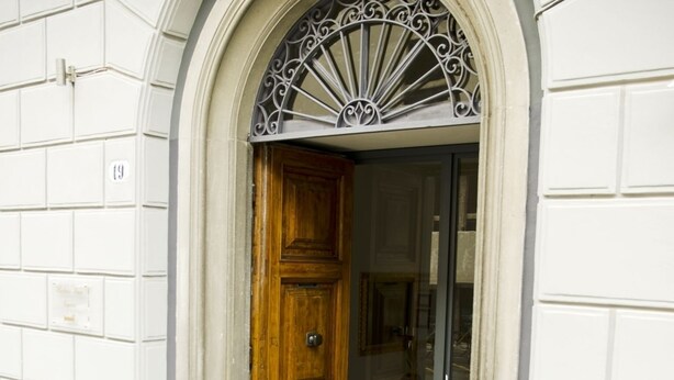 A wooden door with a metal decorative arch above it, flanked by two potted plants. - Relais Inn Lucca (Lucca)