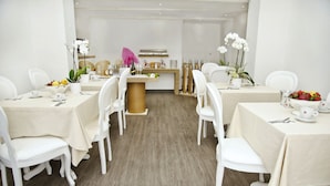 A hotel dining area with white tables and chairs, a central counter with a pink umbrella, and white orchids on the tables. - Relais Inn Lucca (Lucca)