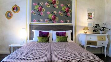 Camera d'albergo con un letto, un comodino, una cassettiera e carta da parati floreale.