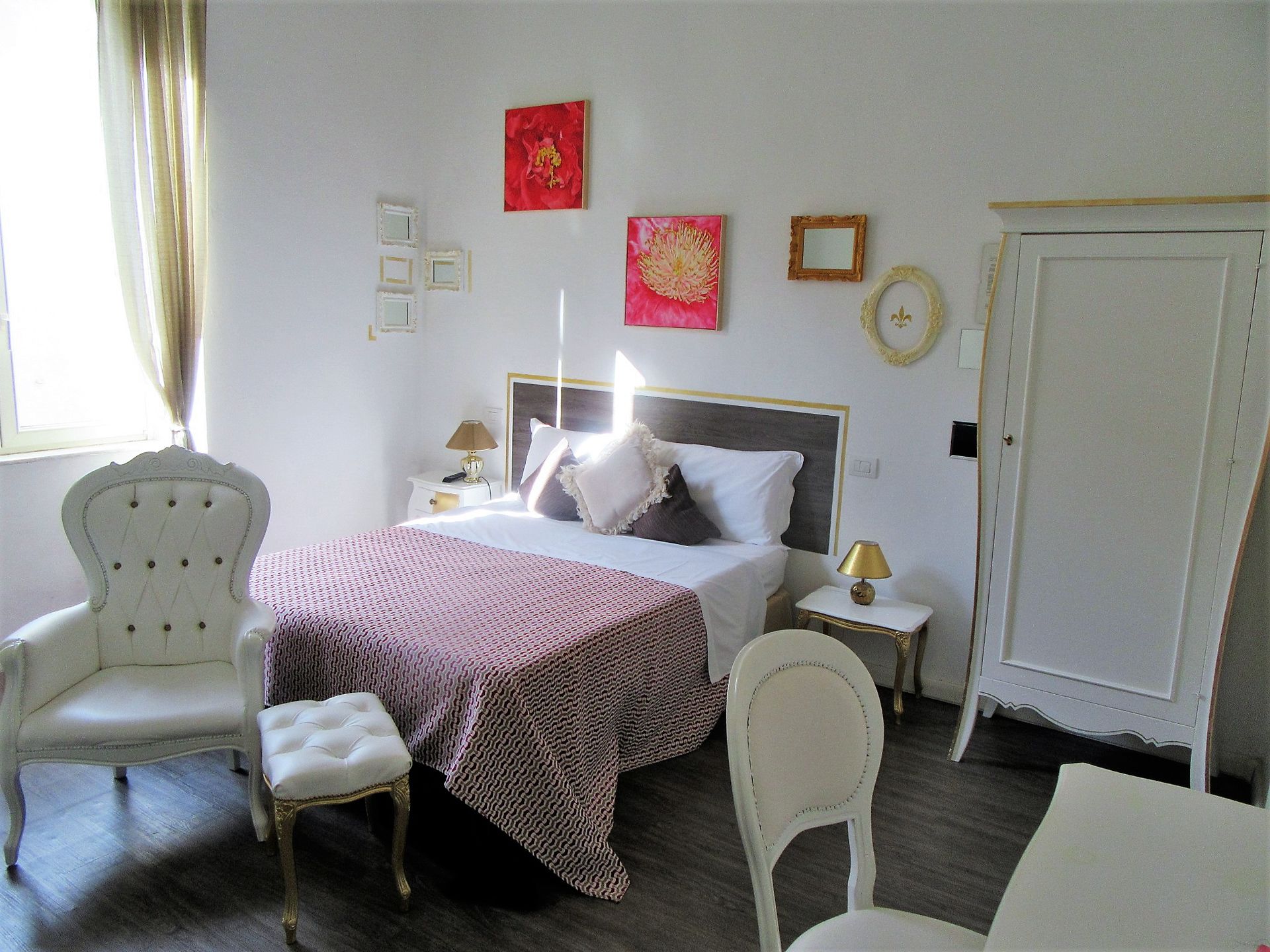 A bedroom with a bed, two bedside tables, a chair, a wardrobe, and decorative wall art.