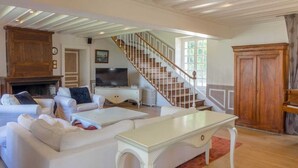 Un salón amplio con un conjunto de sofá blanco, un televisor y una escalera de madera.