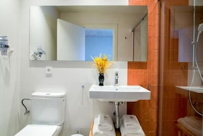 Un baño con inodoro blanco, lavamanos con espejo y zona de ducha.