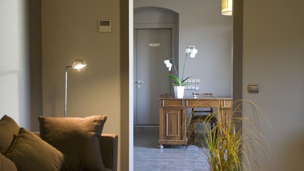 A modern hotel lobby with a sofa, a desk with a potted plant, a lamp, and a door labeled "PRIVAT". - Hostal Barris (Pals)