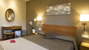 A hotel room with a bed, a desk, a chair, a mirror, a nightstand, a lamp, and a painting on the wall. - Hostal Barris (Pals)