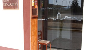 A hotel entrance with a wooden chair outside, a glass door, and a sign reading "HOSTEL BARRIS". - Hostal Barris (Pals)