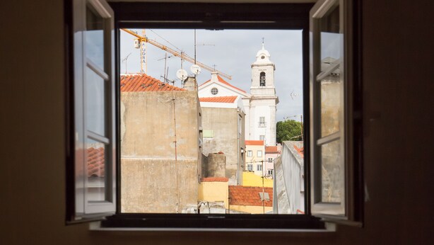 Vista desde una ventana de un edificio con una torre de campanas, una grúa y un tejado de tejas rojas.