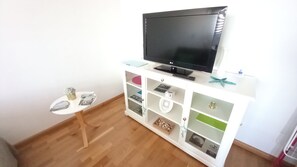 A room with a white entertainment unit, a flat-screen TV, a small round table with a vase and magazines, and a wooden floor. - Beautiful apartment in Salinas (Salinas)