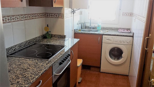 A compact kitchen with a stove, oven, sink, and washing machine.