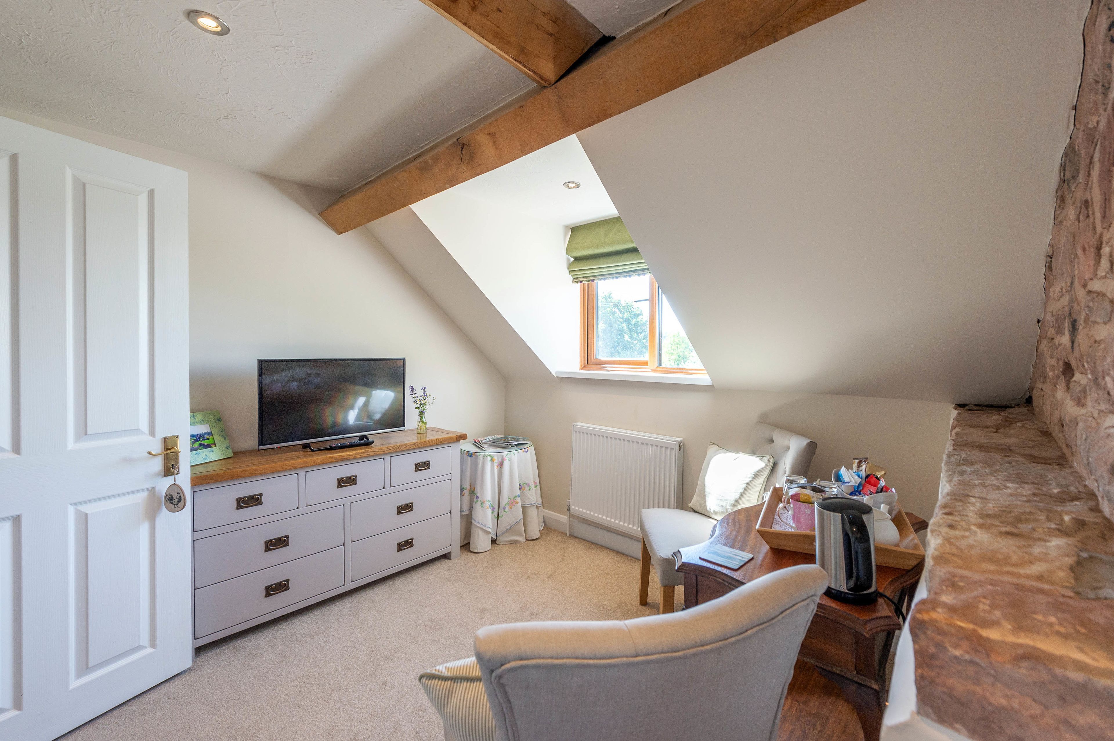 Une chambre mansardée chaleureuse, avec un plafond en pente, un téléviseur posé sur un meuble en bois, un radiateur et un mur en pierre.