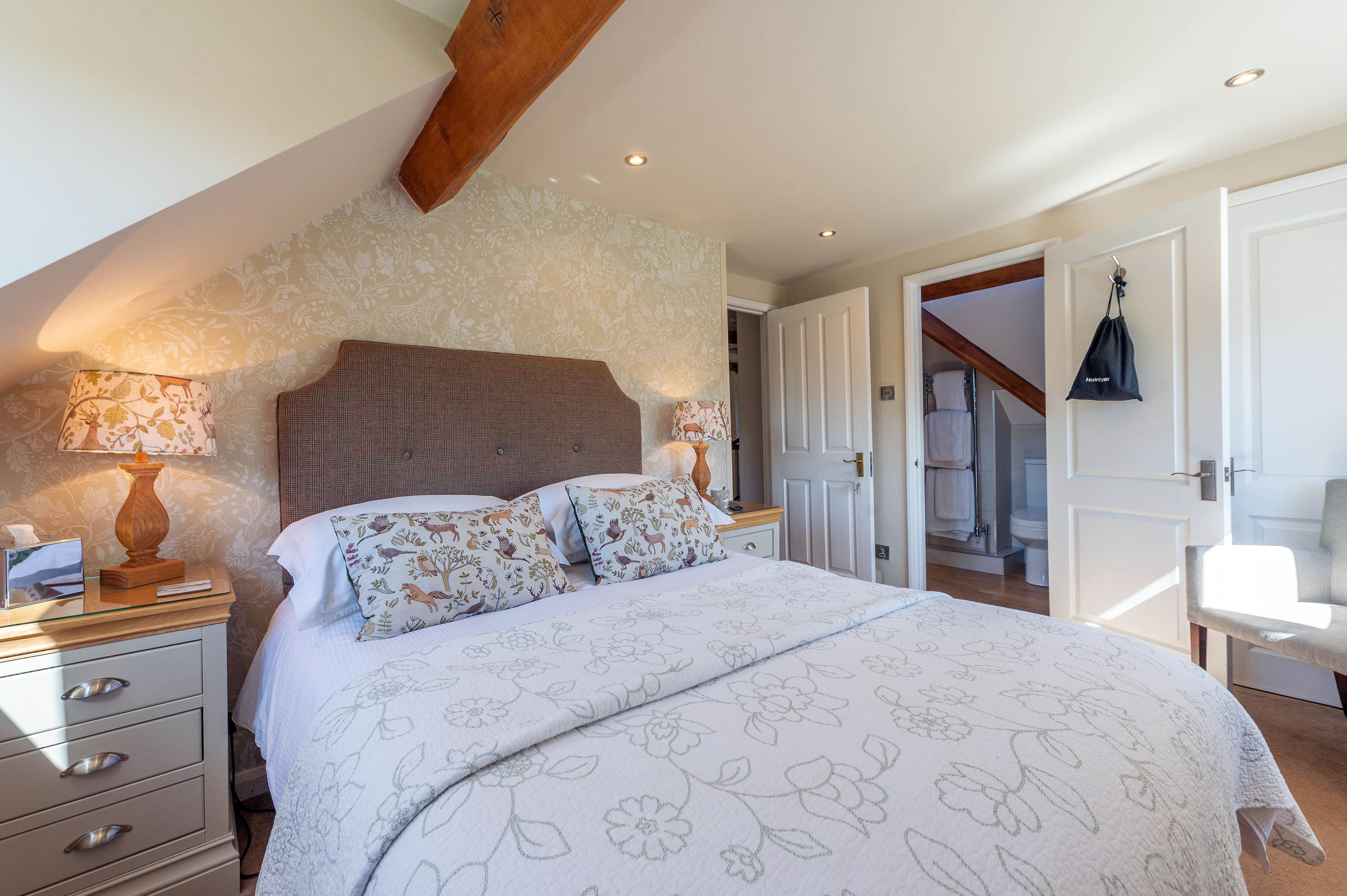 Ein Schlafzimmer mit einem großen Bett, floralem Bettzeug, einem Nachttisch mit Lampe und einem Holzbalken an der Decke.